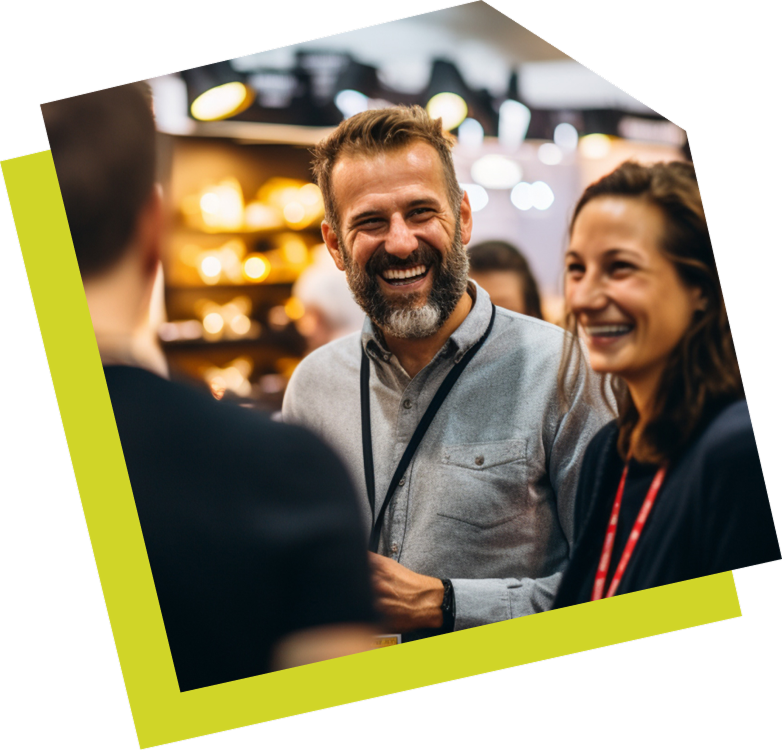 Auschnitt von 2 Personen die sich mit einer anderen Person unterhalten dessen Gesicht von der Kamera abgewandt ist. Die beiden zu sehenden Person lächeln stark