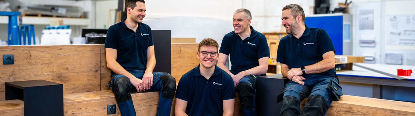 PREUSS MESSE Team Tischler Das Tischler Team der Preuss Messe sitzt in einer aus Holz angefertigten Sitzecke und unterhält sich